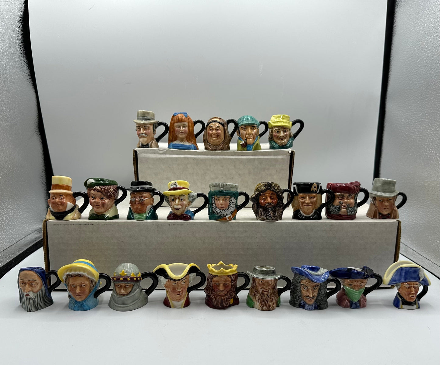 Collection of small ceramic mugs with various facial expressions and hats on a white surface.
