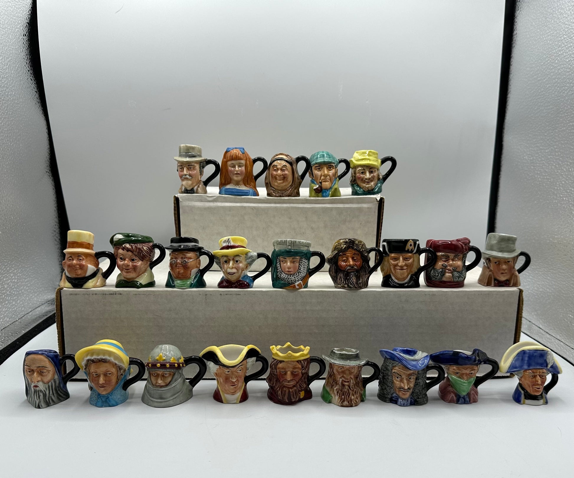 Collection of small ceramic mugs with various facial expressions and hats on a white surface.