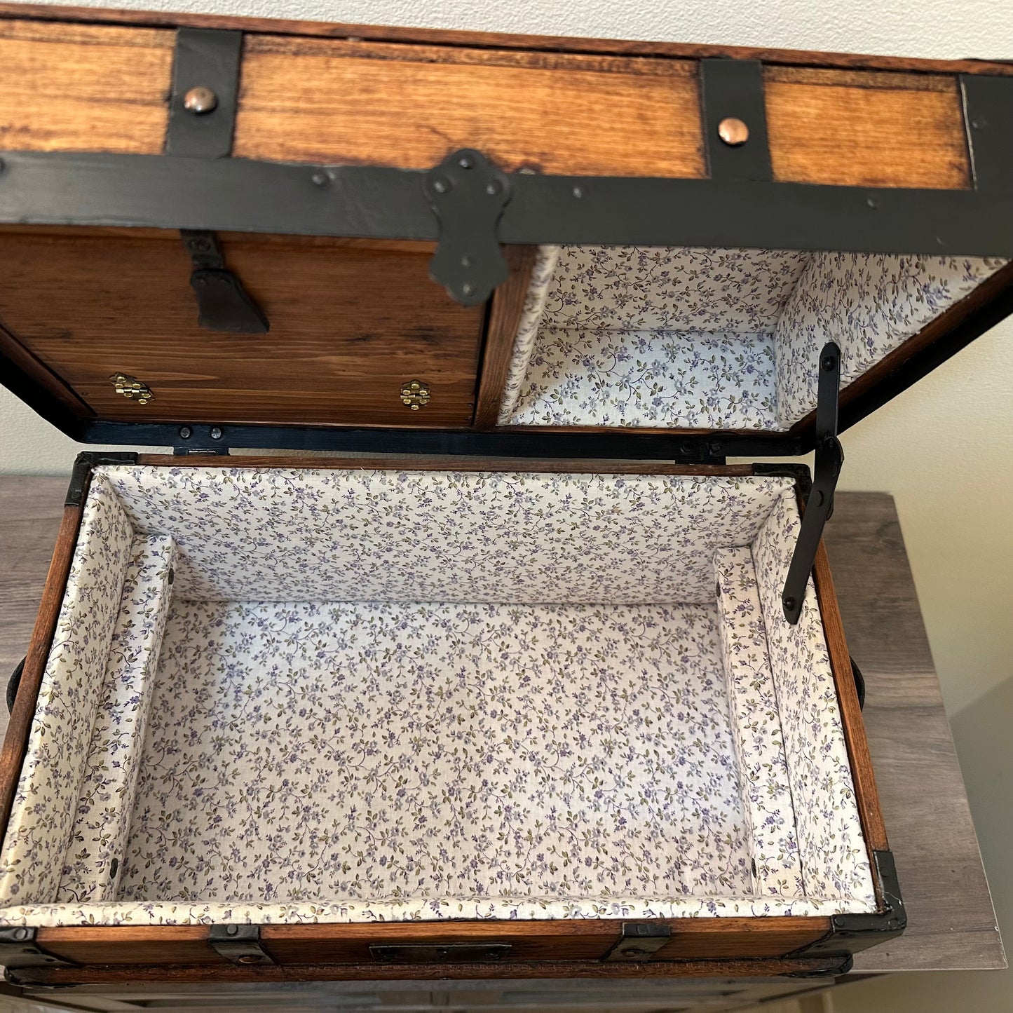 Wooden trunk with floral interior lining on a wooden floor.