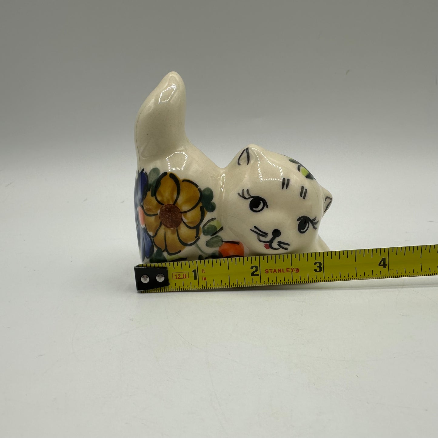Ceramic cat figurine with floral patterns next to a measuring tape on a gray background