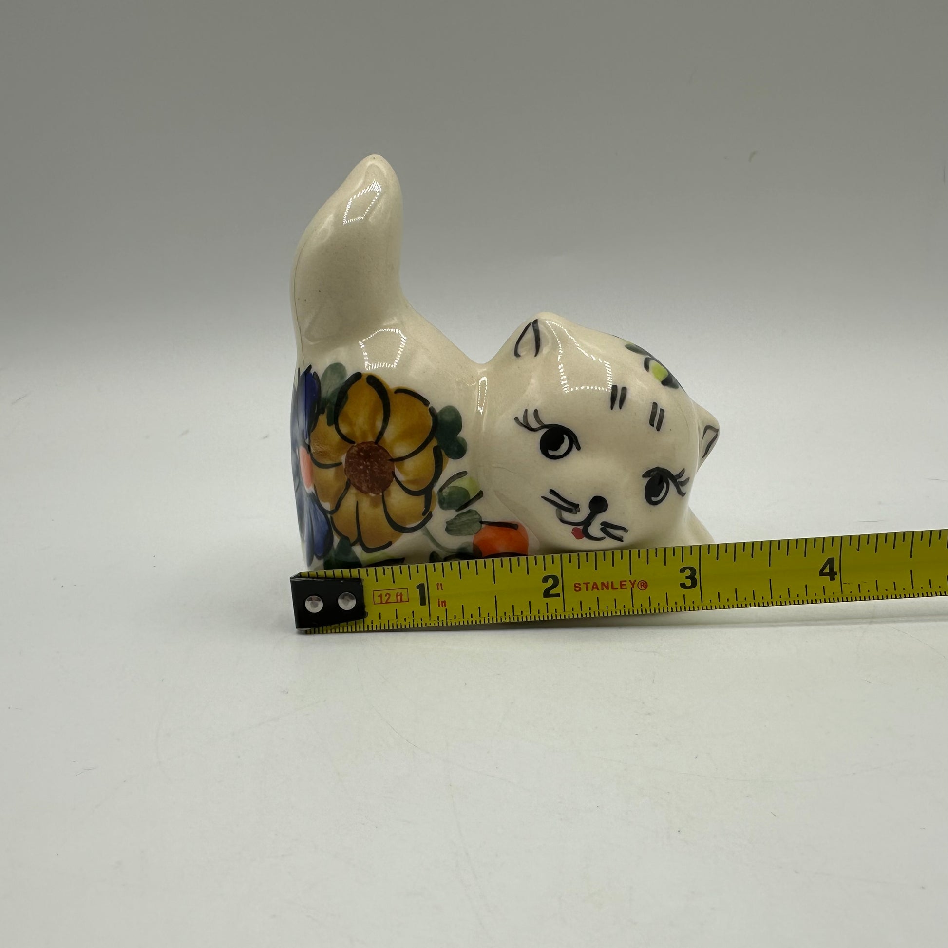 Ceramic cat figurine with floral patterns next to a measuring tape on a gray background