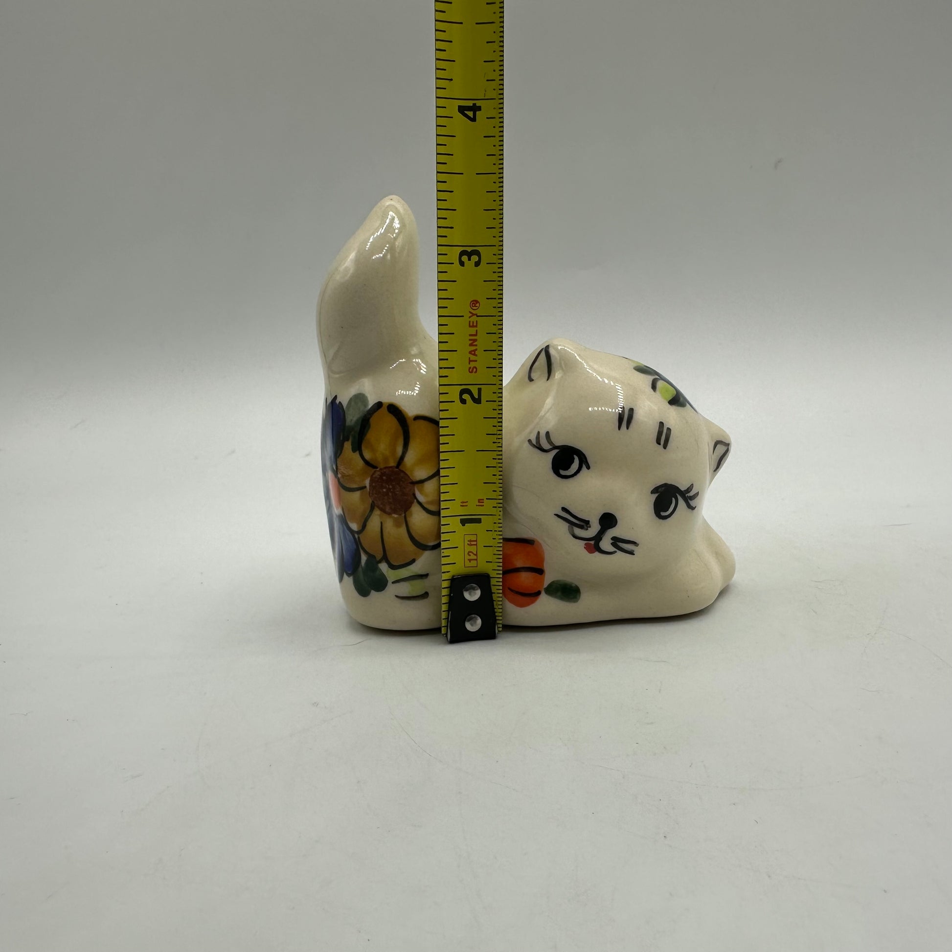 Ceramic cat figurine with floral design next to a ruler on a gray background