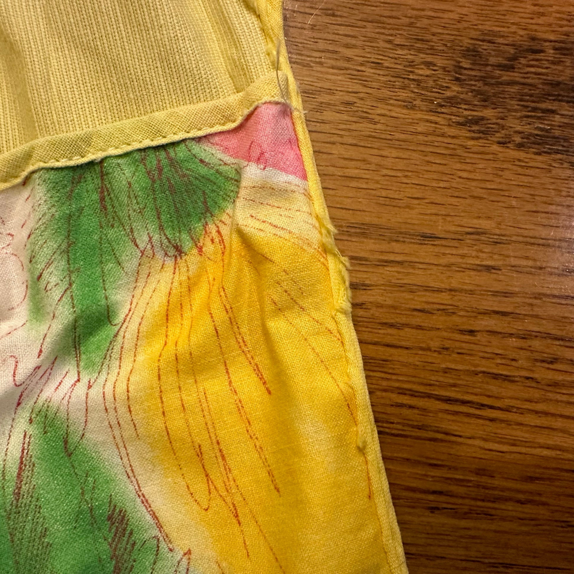 Close-up of a colorful fabric with yellow, green, and pink patterns on a wooden surface.