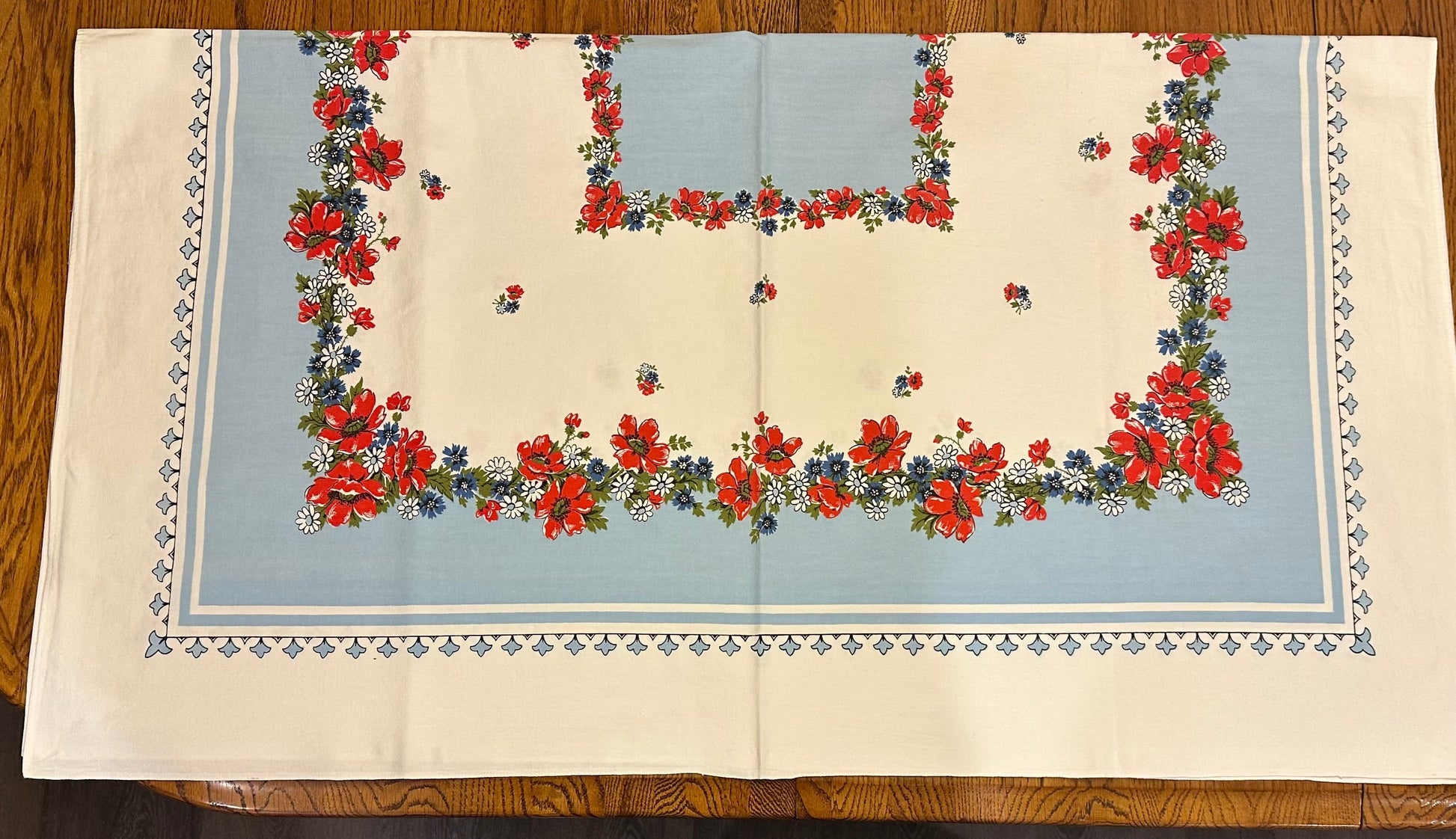 Floral patterned tablecloth with red flowers and blue background on a wooden surface