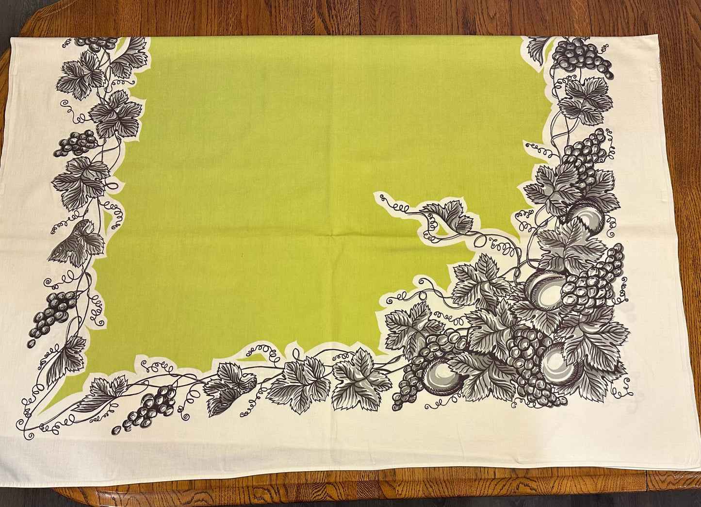 Decorative tablecloth with black floral and fruit pattern on a wooden table.